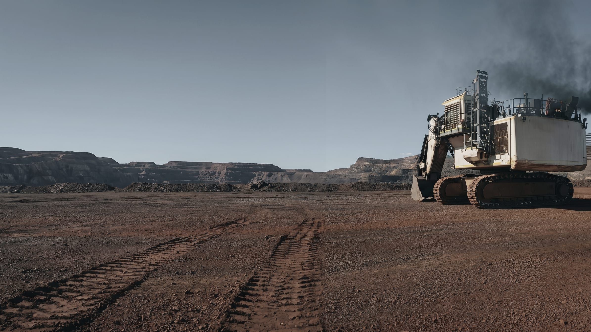 Mining excavator working on a red-dirt bench, mesa country behind